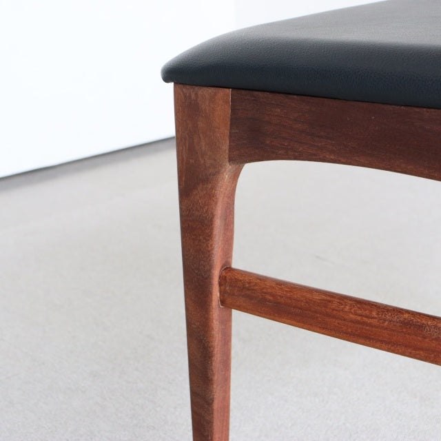 Close-up of vintage teak dining chair leg and frame with smooth wood grain and black faux leather seat from British.