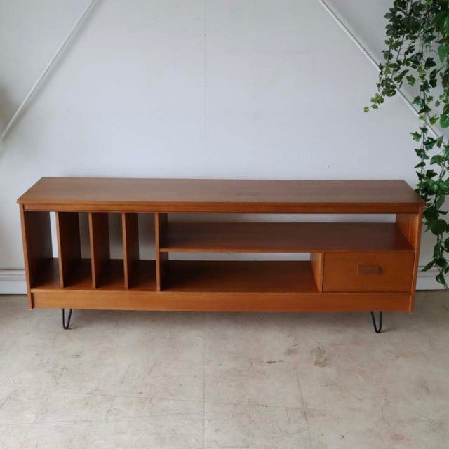 Mid-century British vintage teak TV board with open shelving, vertical dividers, single drawer, and slender iron hairpin.