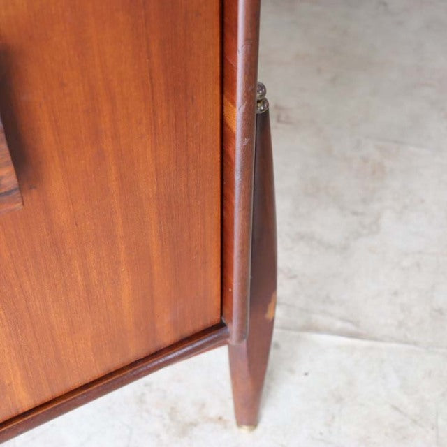 Close-up of vintage British mid-century teak sideboard leg with rich wood grain and tapered design on light floor.