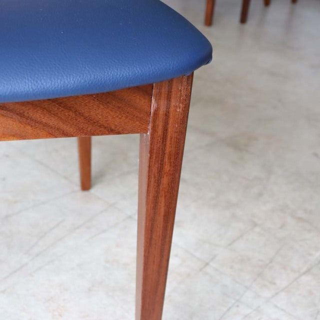 Close-up of vintage G-PLAN Fresco dining chair leg in polished teak with visible wood grain and navy blue upholstered seat.