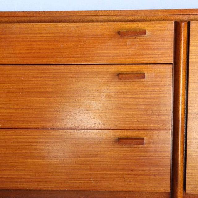 Close-up of vintage teak sideboard drawers with smooth wood grain and minimalist rectangular handles, mid-century British.