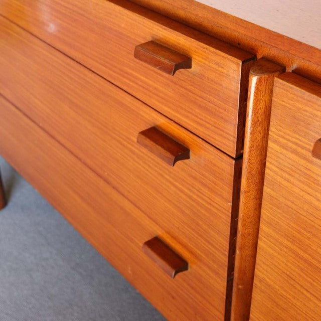 Mid-century British vintage teak sideboard with rich wood grain, rectangular wooden handles, and tapered legs.