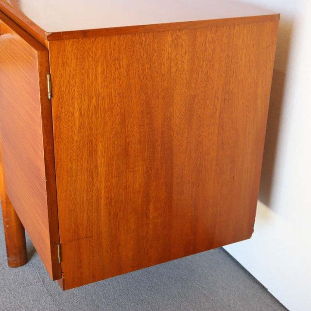 Vintage teak British mid-century sideboard showing rich wood grain and sturdy straight legs, smooth door panel with brass.