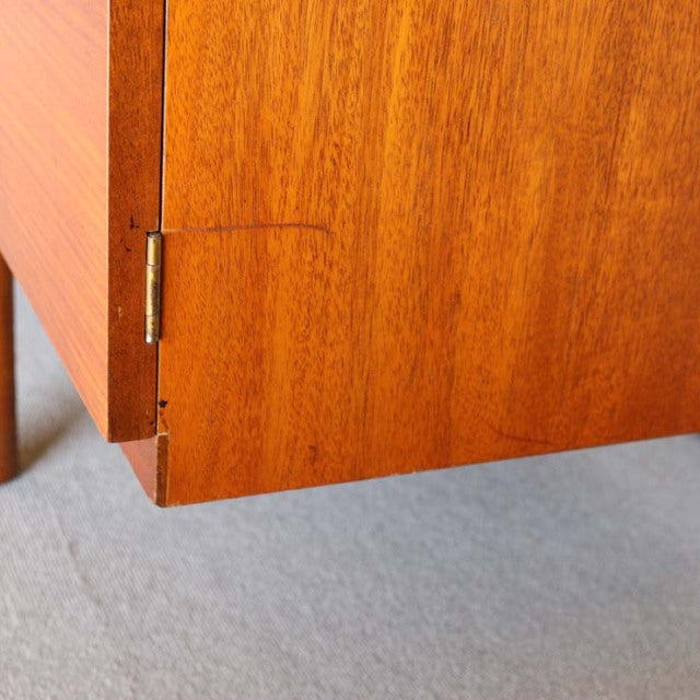 Close-up of mid-century British vintage teak sideboard corner showcasing warm wood grain, brass hinge, and clean lines on.