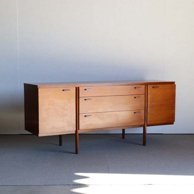 Mid-century British vintage teak sideboard with clean lines, three central drawers, and two side cabinets on slender legs.