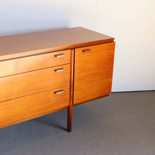 Mid-century British vintage teak sideboard with smooth grain, three drawers, and a single door on slender legs.