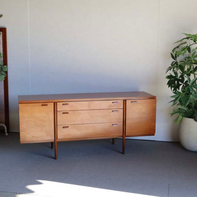 Vintage teak sideboard in British mid-century style with clean wood grain, three central drawers, and smooth curved edges,.