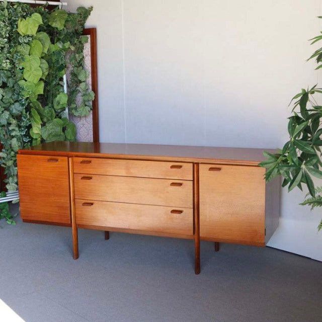 Mid-century British vintage teak sideboard with warm wood grain, sleek tapered legs, and minimalist handles.