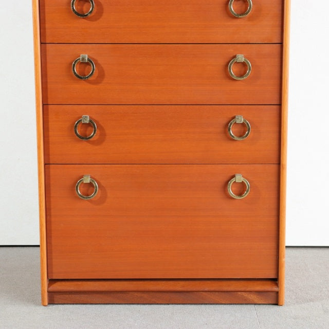 Vintage British mid-century teak chest with smooth wood grain, four drawers, and round brass ring handles.