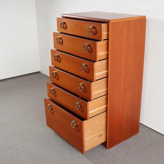 Vintage British mid-century teak chest with six drawers, brass ring handles, clean lines, and tapered legs, showcasing rich.