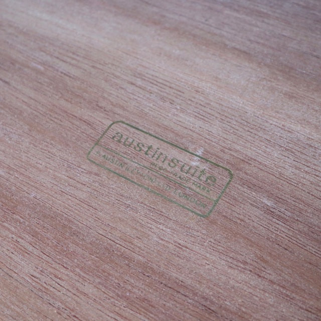 Close-up of vintage Austinsuite teak wood surface showing smooth grain and stamped brand logo, mid-century British-Danish.