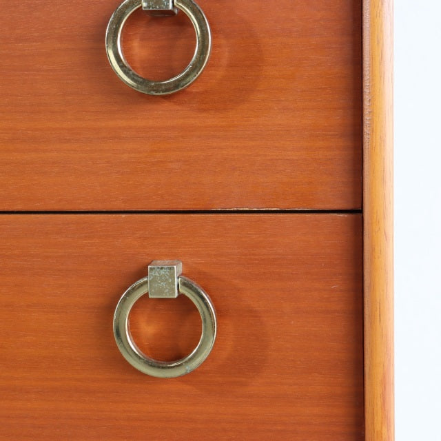 Close-up of vintage British mid-century teak chest drawer with brass ring pulls and smooth wood grain detailing.