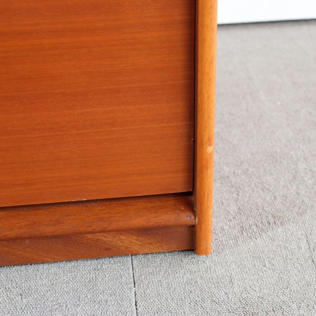 Close-up of vintage teak mid-century British chest corner showing smooth wood grain and rounded leg detail on a neutral floor.