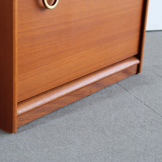 Mid-century British vintage teak chest corner showing smooth wood grain and rounded base detail on carpeted floor.