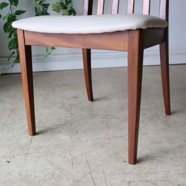 Mid-century vintage British teak dining chair with ivory upholstered seat, sleek tapered legs, and smooth wood grain.