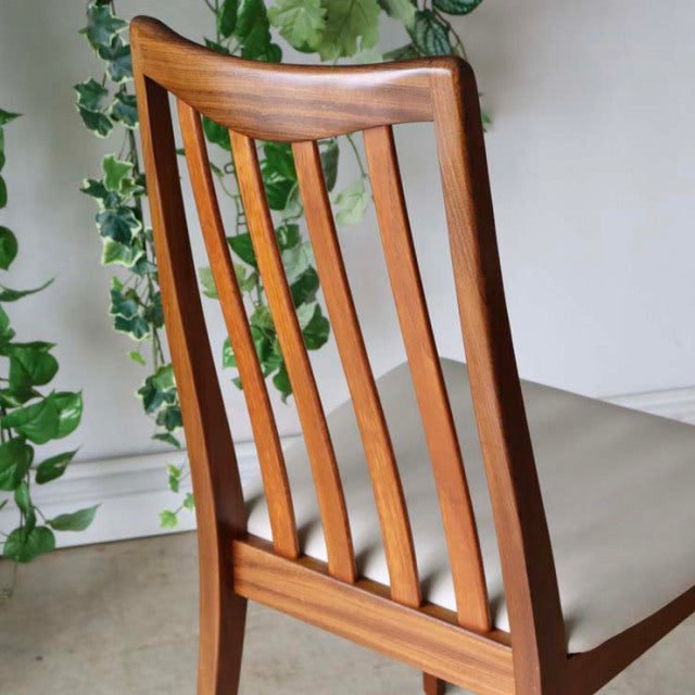 Set of four vintage British mid-century teak dining chairs with ivory upholstered seats and curved slatted backs.