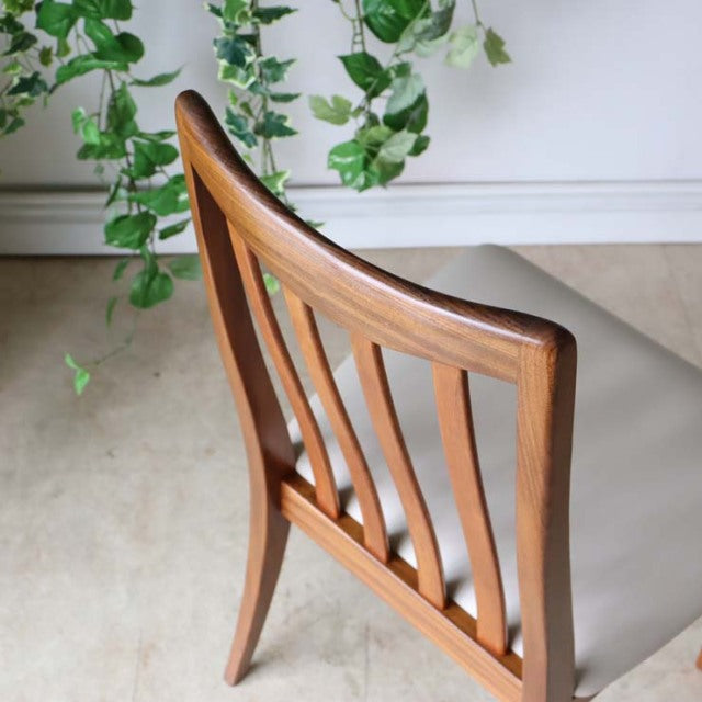Mid-century British vintage teak dining chair with curved slat back and ivory cushioned seat.