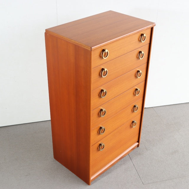 Vintage mid-century British teak chest with seven drawers, brass ring handles, clean wood grain, and tapered legs.