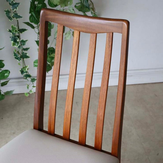 Mid-century British vintage teak dining chair with vertical slats and ivory upholstered seat, sleek tapered legs.