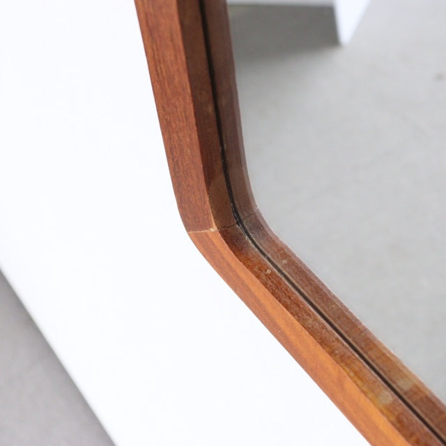 Close-up of vintage mid-century British teak trapezoid wall mirror frame with smooth wood grain and beveled edges.