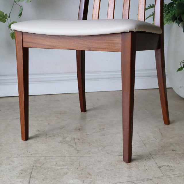 Set of four vintage British mid-century teak dining chairs with ivory upholstered seats and tapered legs.