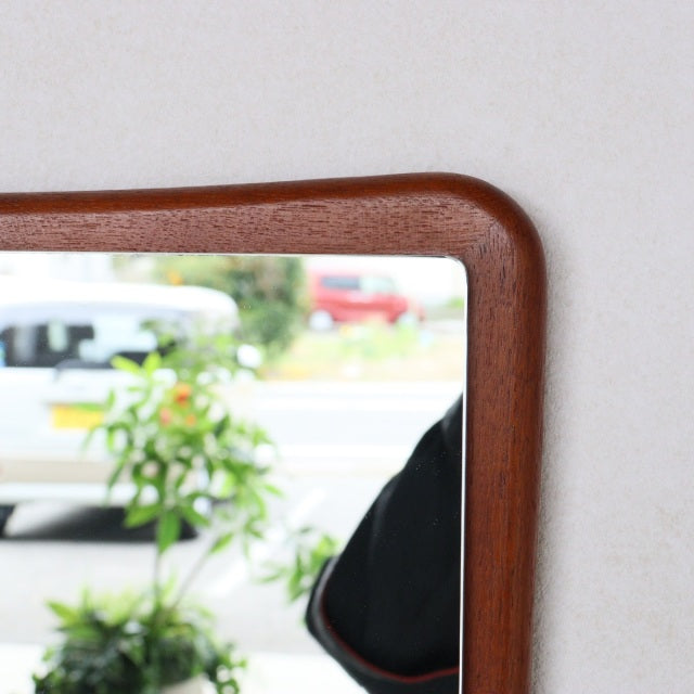 Mid-century British vintage teak wall mirror with gently curved edges and smooth wood grain finish.