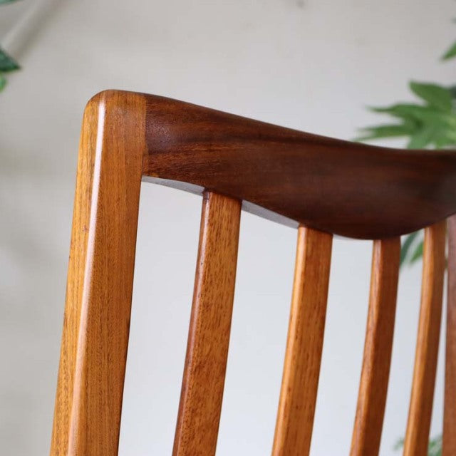 Close-up of vintage mid-century teak dining chair backrest with smooth dark upper rail and vertical lighter wood slats,.