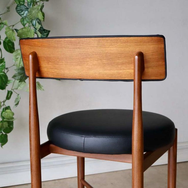 Set of four vintage G-Plan teak dining chairs with mid-century British design, black leather seats, and sleek tapered legs.