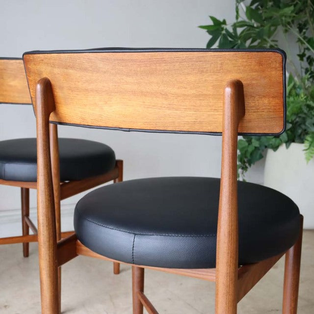 Set of four vintage G-Plan mid-century teak dining chairs with black leather cushions and curved wooden backs.