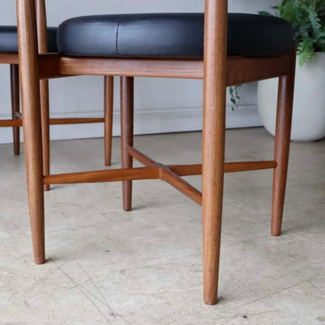 Set of four British mid-century G-plan dining chairs in vintage teak with black leather seats and tapered legs.
