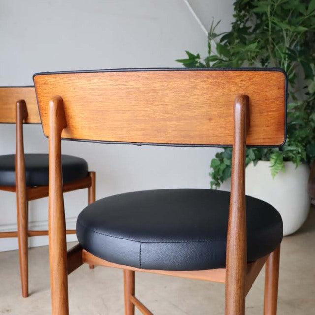 Set of four vintage British G-Plan Fresco dining chairs in teak with rounded black leather seats and slender tapered legs,.
