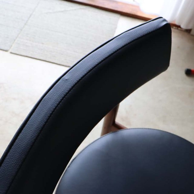 Close-up of vintage British G-plan mid-century teak dining chair with black curved leather backrest and seat, smooth wood.