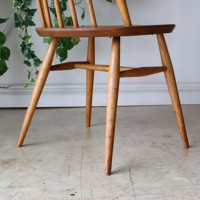 Vintage Ercol Goldsmith high-back chair in natural teak with tapered legs and visible wood grain, British mid-century design .