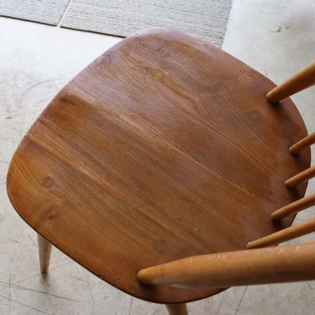 Vintage British Ercol Goldsmith chair with smooth teak seat, mid-century curved edges, and slender spindle backrest legs in.