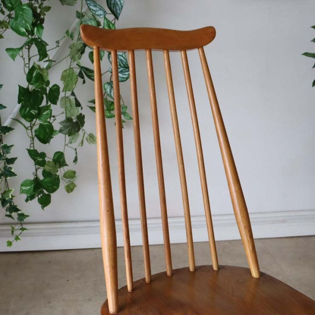 Mid-century British Ercol Goldsmith dining chair in teak with natural wood grain, slender spindle backrest, and curved top.