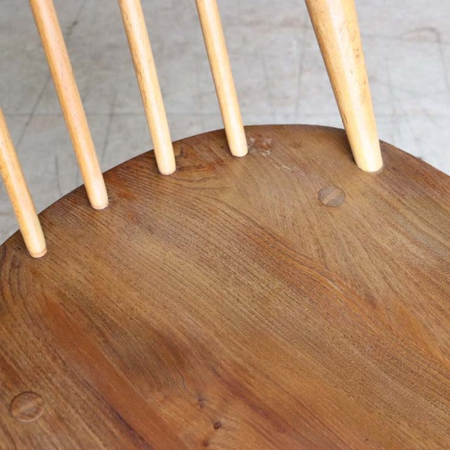 Close-up of vintage British Ercol Goldsmith dining chair seat in warm teak with smooth wood grain and slender spindle back.