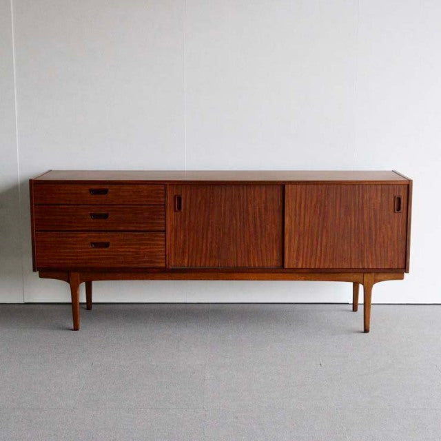 Mid-century British vintage teak sideboard by Nathan with smooth grain, three drawers, sliding doors, and slender tapered.