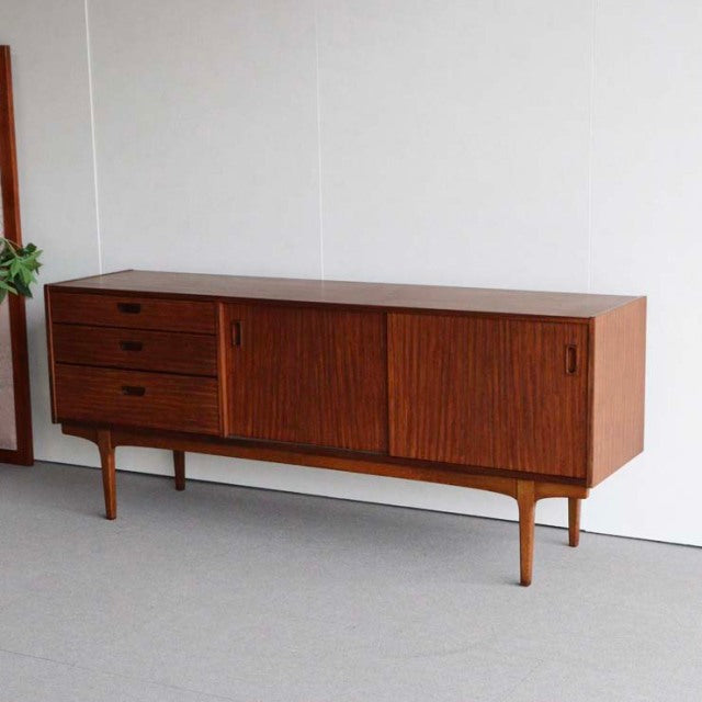 Mid-century teak sideboard by Nathan with rich wood grain, three drawers on left, sliding doors on right, and slender.