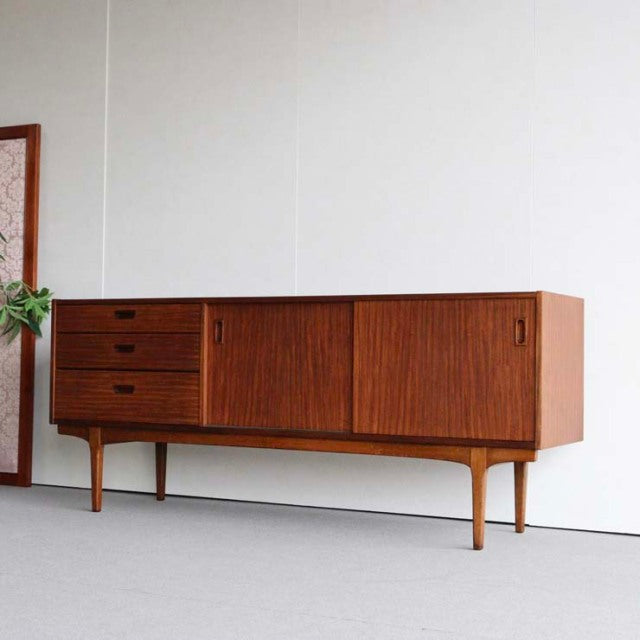 Mid-century British vintage teak sideboard by Nathan with three drawers, sliding doors, tapered legs, and fine wood grain.