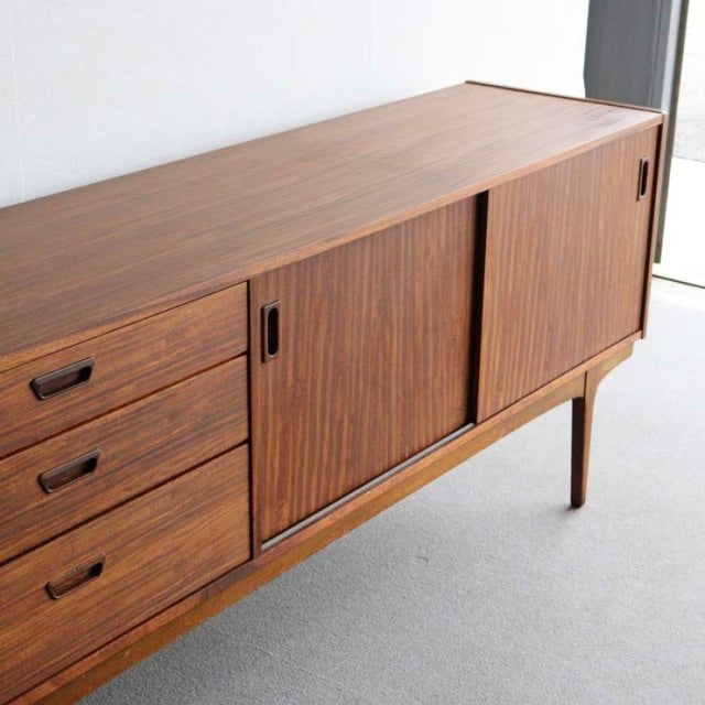 Mid-century vintage teak sideboard by British brand Nathan, featuring sliding doors, three drawers, and tapered legs with.
