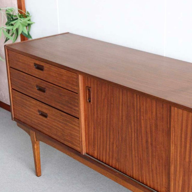 Vintage mid-century teak sideboard by British brand Nathan with three drawers on left and sliding door on right, showcasing.