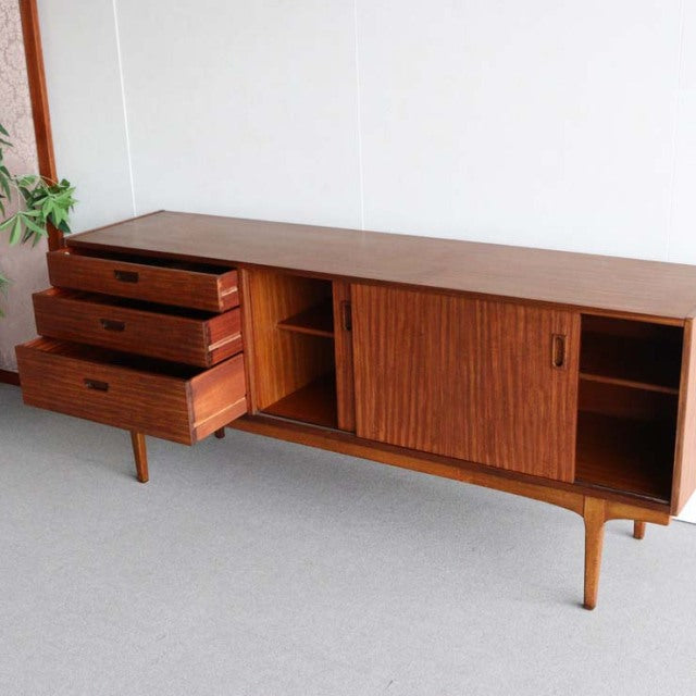 Vintage teak mid-century British sideboard by Nathan with three drawers, sliding doors, and tapered legs.
