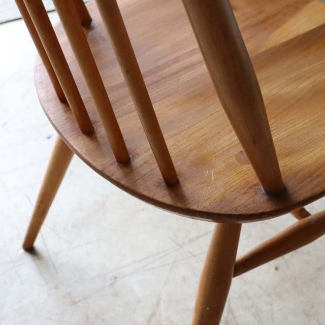 Vintage British mid-century teak dining chair with smooth rounded seat, slender spindle backrest, and tapered legs.