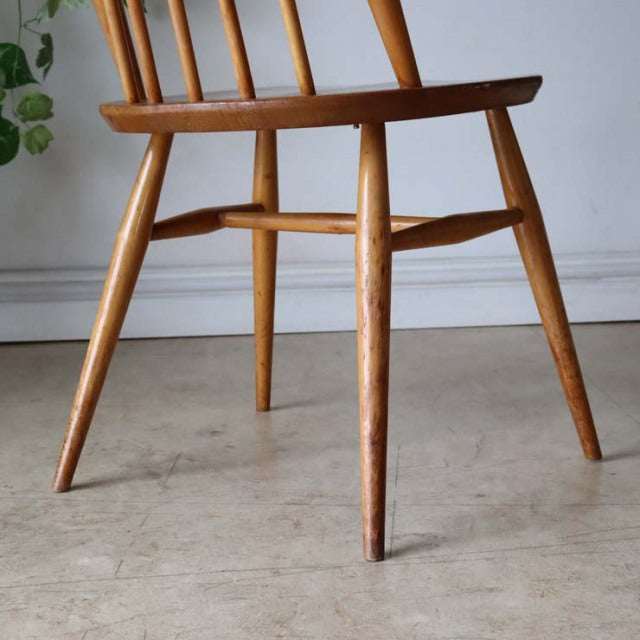 Vintage Ercol Goldsmith high-back dining chair in natural teak with slender tapered legs and visible wood grain, mid-century .