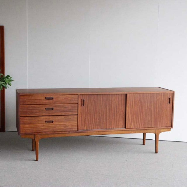 Vintage mid-century teak sideboard by Nathan from Britain with sliding doors, three drawers, and slender tapered legs.
