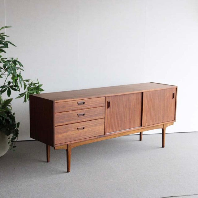 Mid-century British teak sideboard by Nathan with clean lines, three drawers on left, sliding doors on right, angled legs,.