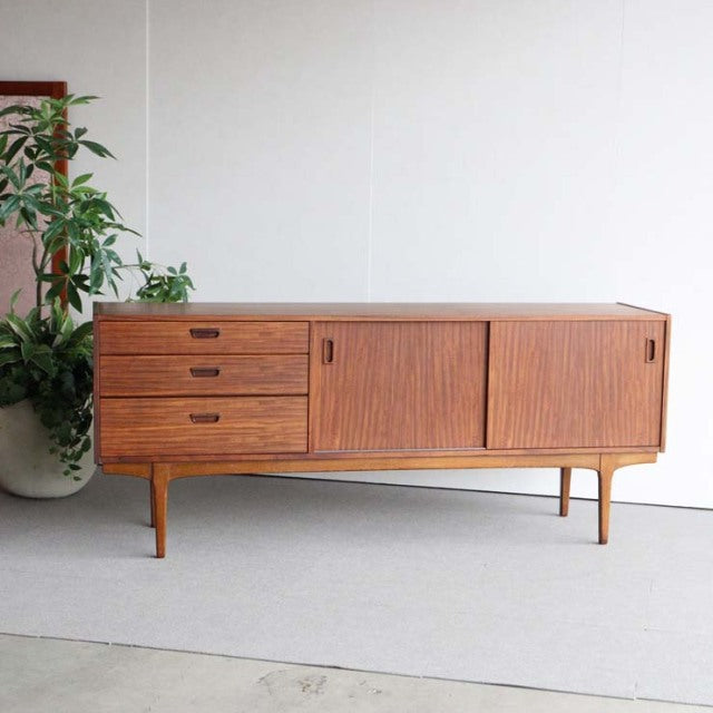 Mid-century British vintage teak sideboard by Nathan with three drawers and sliding doors on slender tapered legs.