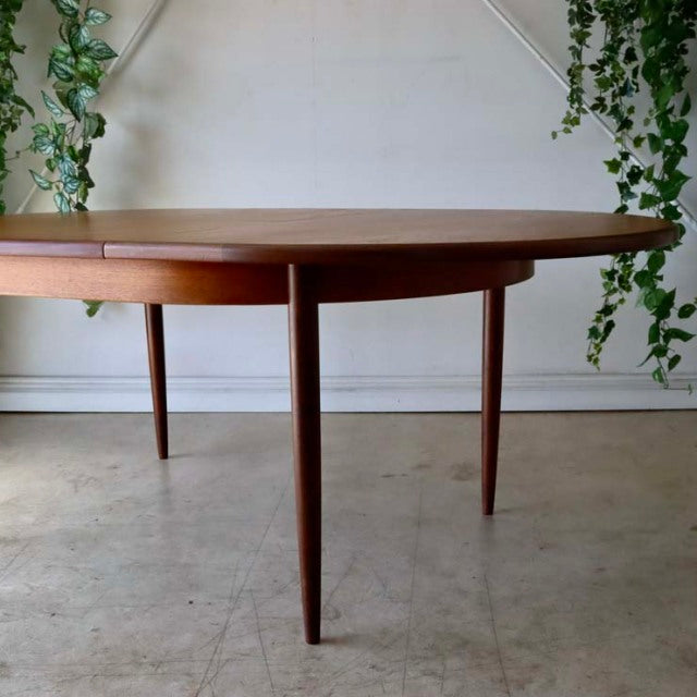 Vintage British mid-century teak dining table by G-Plan with oval top and slender tapered legs, smooth wood grain finish.