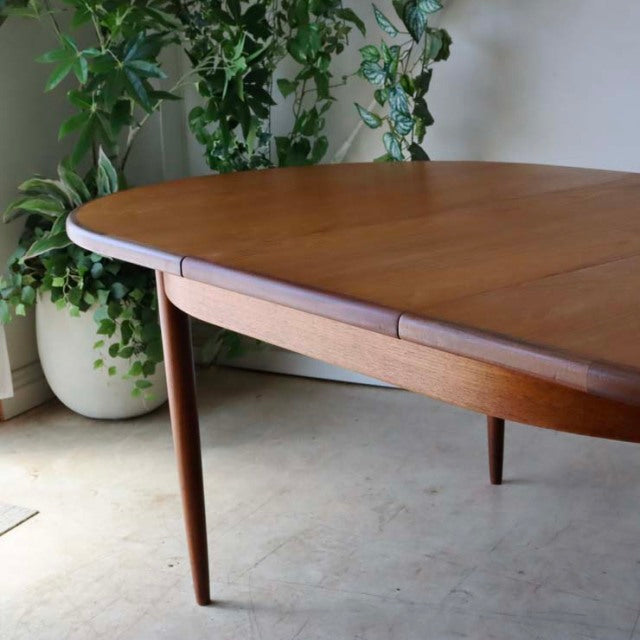 Vintage mid-century British G-Plan dining table in teak with oval top and tapered legs, smooth wood grain finish.