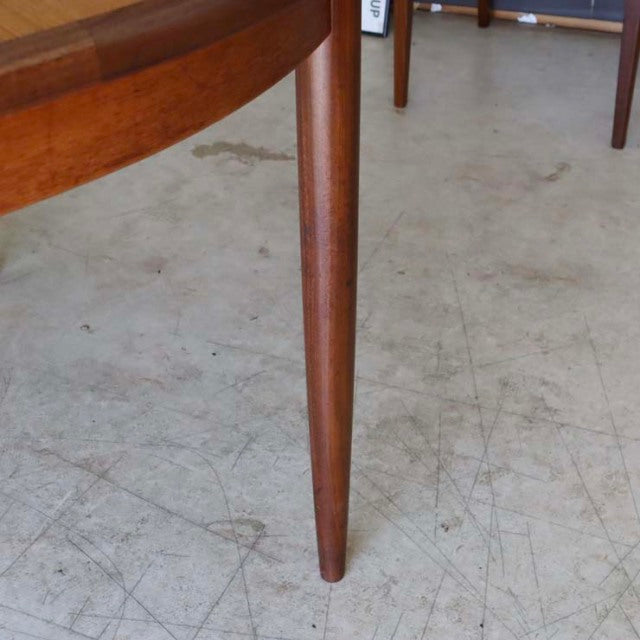 Mid-century British vintage teak dining table leg with smooth wood grain and tapered cylindrical shape on concrete floor.